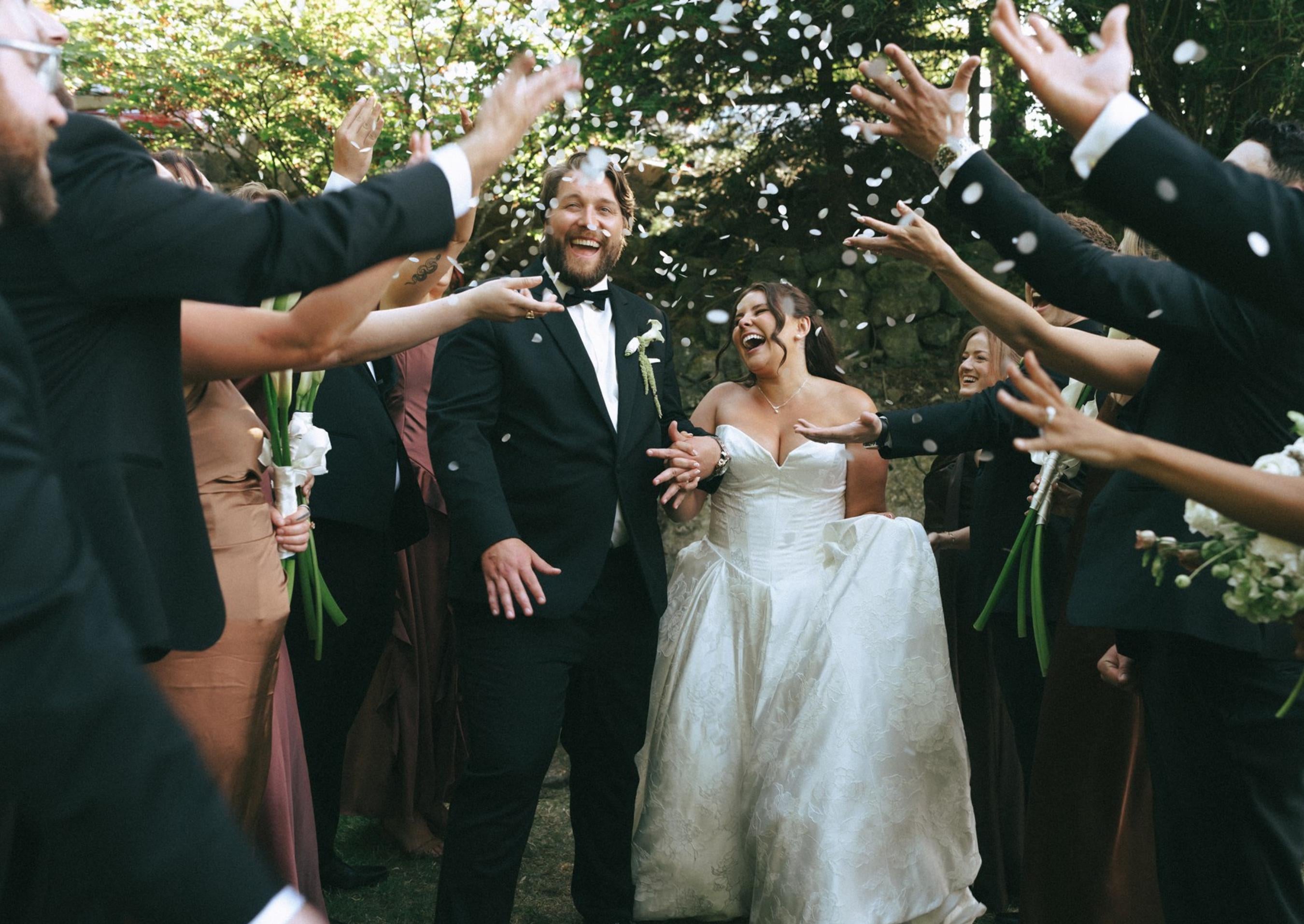 Wedding party throwing white biodegradable confetti over a laughing bride and groom